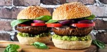 Portobello mushroom vegan burgers with avocado, tomato and spinach and onion on a wood serving board against a dark brick background