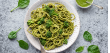 photograph of spinach pesto pasta on a dish surrounded by spinach leaves