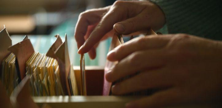 Close-up of female hands browsing old card catalog drawers, vintage library research concept