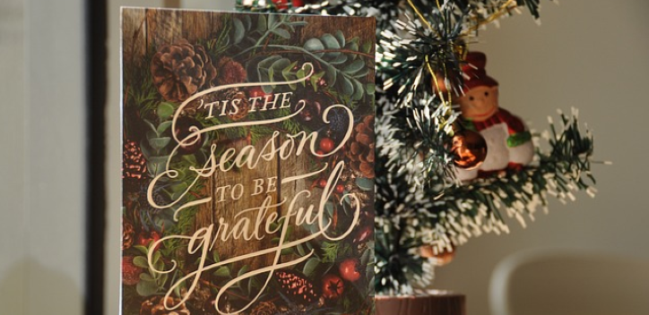 A Christmas card on a table with a miniature Christmas tree behind
