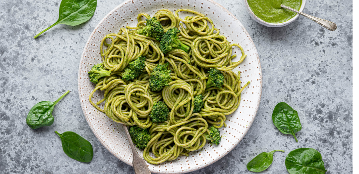 photograph of spinach pesto pasta on a dish surrounded by spinach leaves