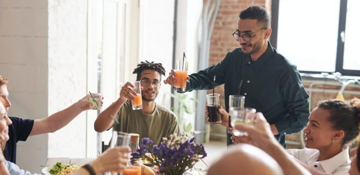 image of friends sitting around a table eating food and raising a toast