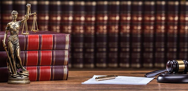 A desk with legal books, a statue of Lady Justice and a gavel.