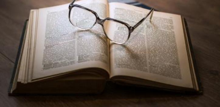An open book with glasses resting on top.