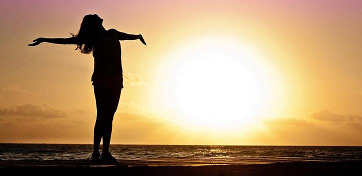 A photograph of a person standing with arms spread wide, in front of a sunset