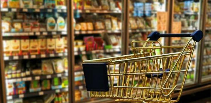 A shopping trolley to the forefront with a row of fridges containing food in the background.