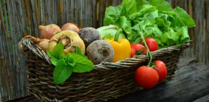 A long backet full of vegetables and greens sitting on a wooden bench.