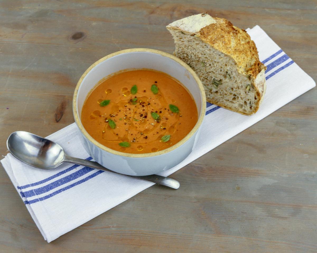 Bowl of gazpacho and bread on top of a tea cloth with a metal spoon