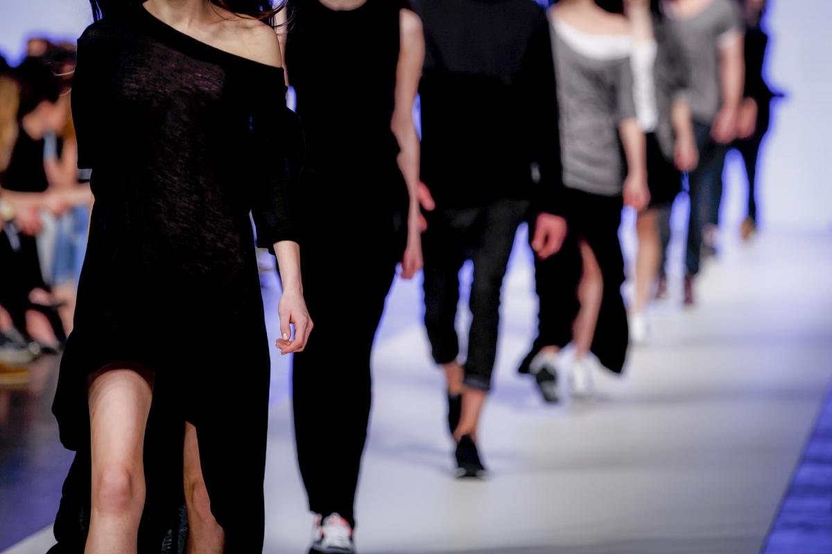 Model on catwalk photographed from the neck down with other models walking behind