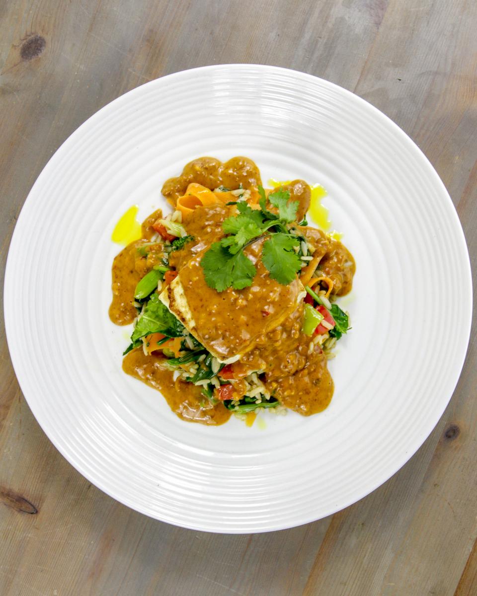 vegan satay tofu and spring onion rice with green garnish on a white plate against a grey background