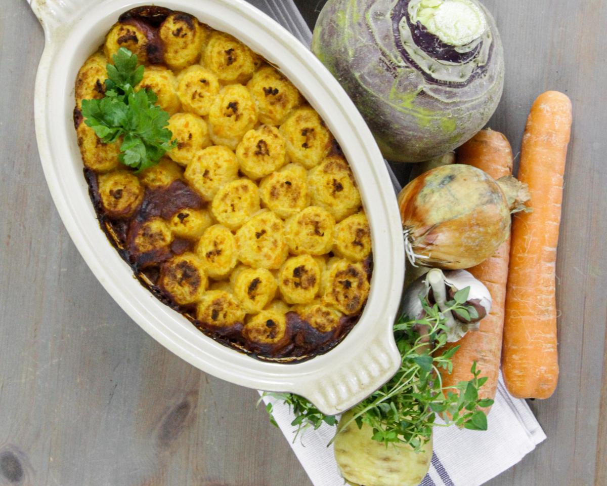 Lentil shepherds pie in an oval dish with a green garnish with onion, carrots and garlic to decorate