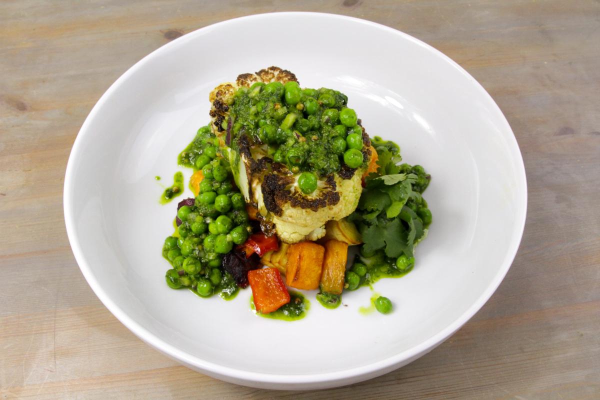 vegan cauliflower steaks with chimichurri peas on a white plate against a grey background