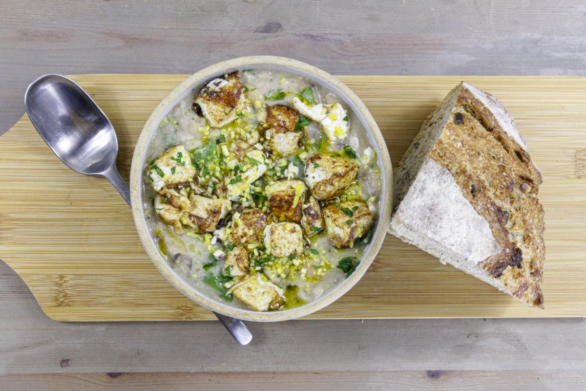 vegan white bean cassoulet and tofu gremolata in a round bowl with a silver spoon to the left