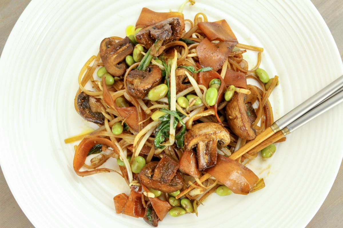 Close up of vegan noodles, mushrooms, peas and beansprouts on a white dish