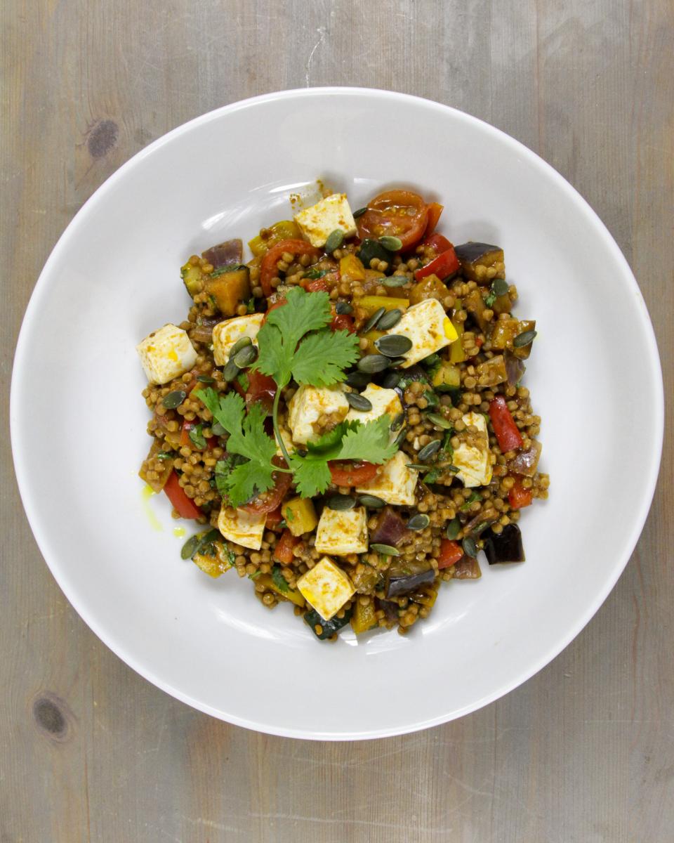 vegan Moroccan-spiced tofu and giant couscous on a white plate against a grey background