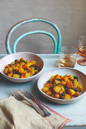 Two bowls of orange coloured pumpkin gnocci on a dining table with two forks on a tea towel and two drinks