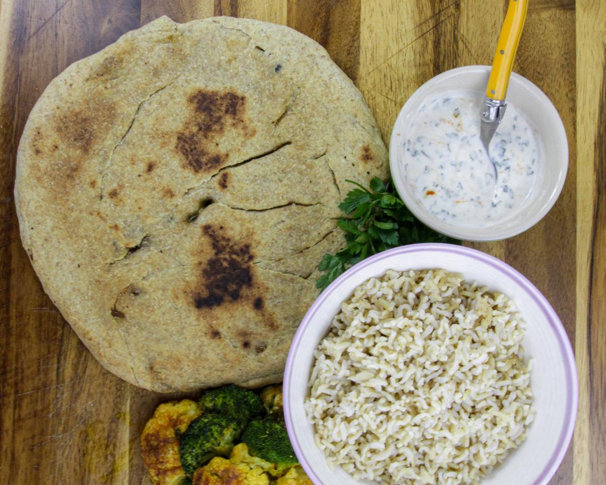 vegan baked katlama round bread on a wooden board with a white dipping sauce and a bowl of rice