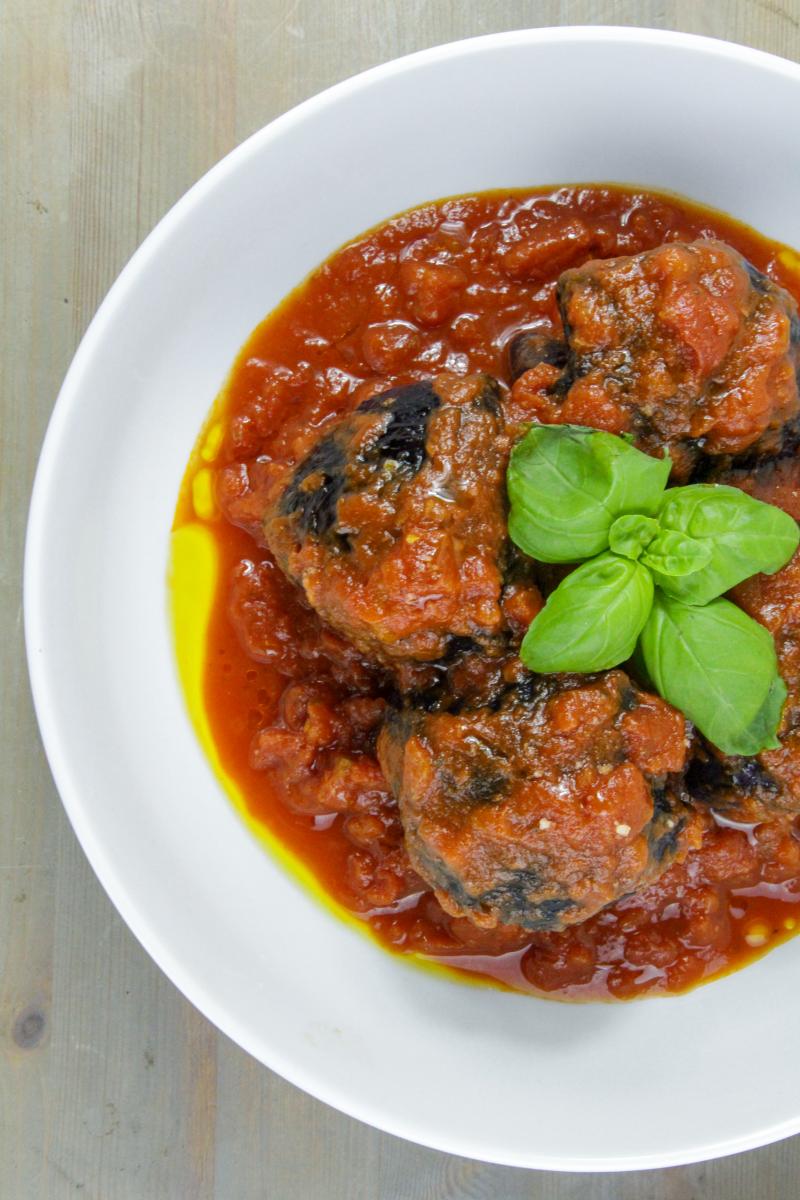 vegan baked stuffed cabbage parcels with tomato and chilli with a basil garnish in a white bowl on a grey background