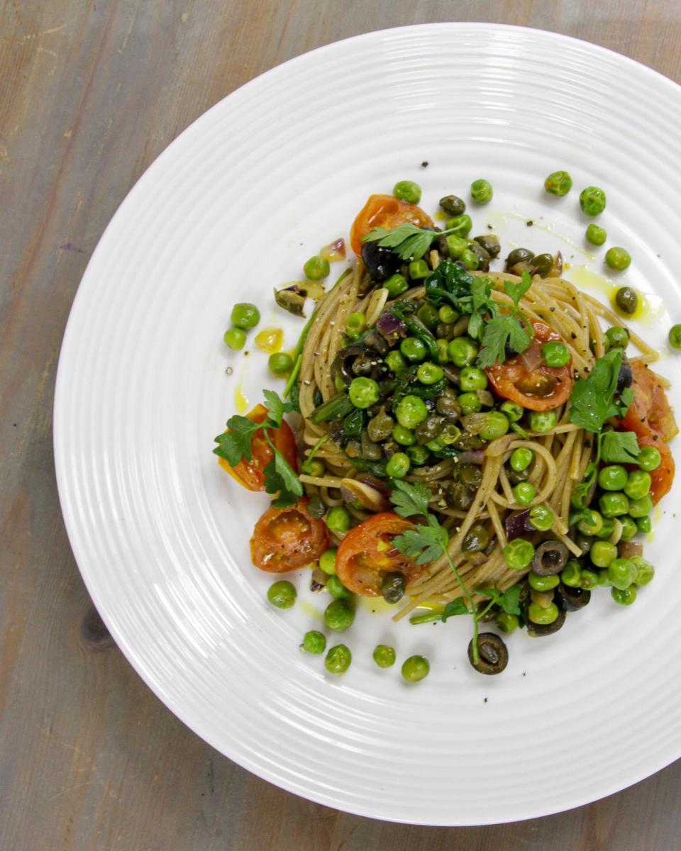 vegan wholewheat spaghetti with garlic, capers and parsley on a white dish against a grey background