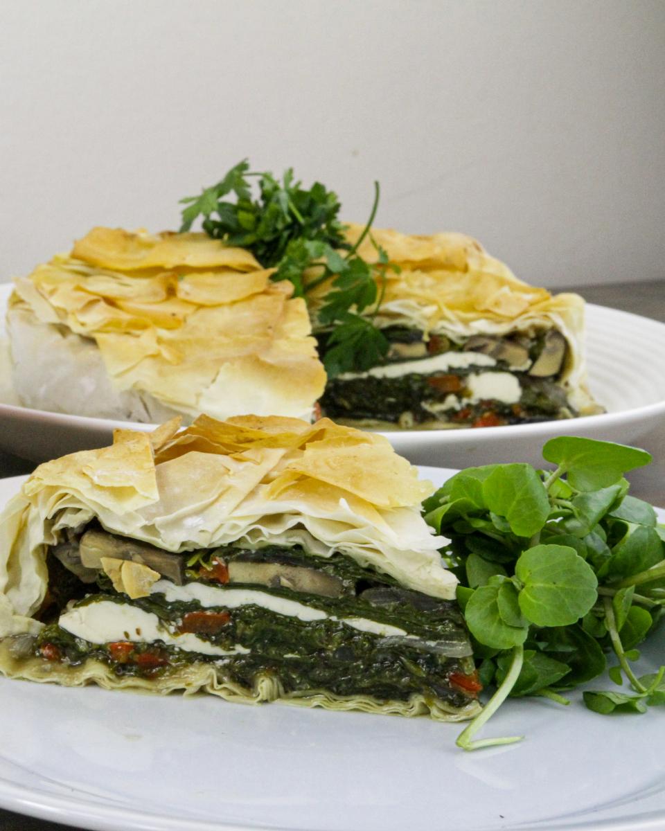 a serving of vegan tofu and spinach spanakopita with the full bowl of food behind