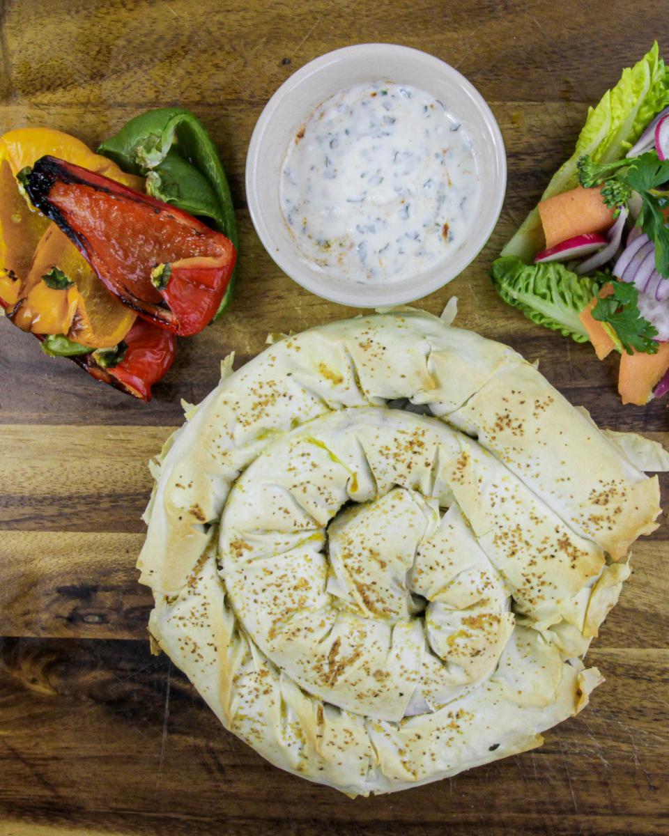 Bosnian burek bread on a wooden board with fried peppers, white herb sauce and salad