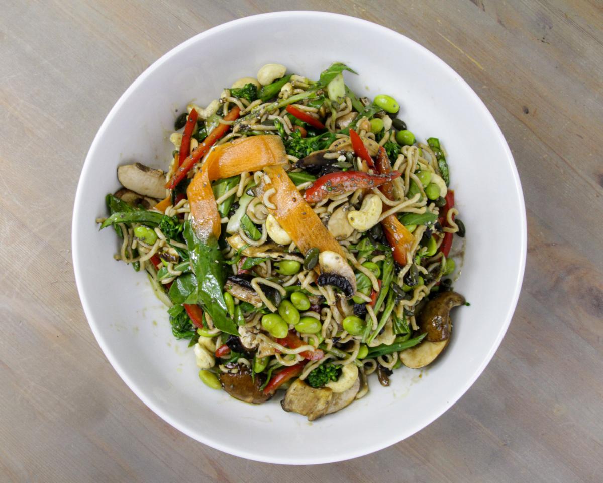 vegan mushroom, cashew and radish noodles with veg in a white bowl on a grey surface