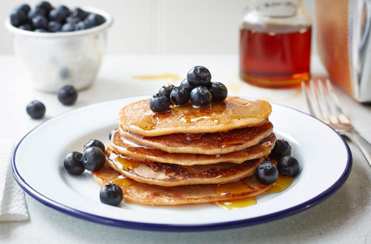 A stack of banana pancakes topped with blackberries, served on a circular plate.