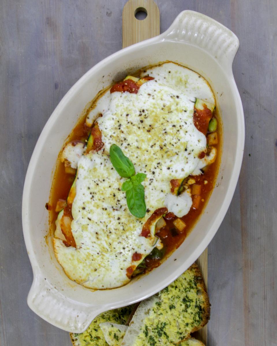 vegan carrot and courgette cannelloni in a white oval oven dish on a wooden board against a grey background