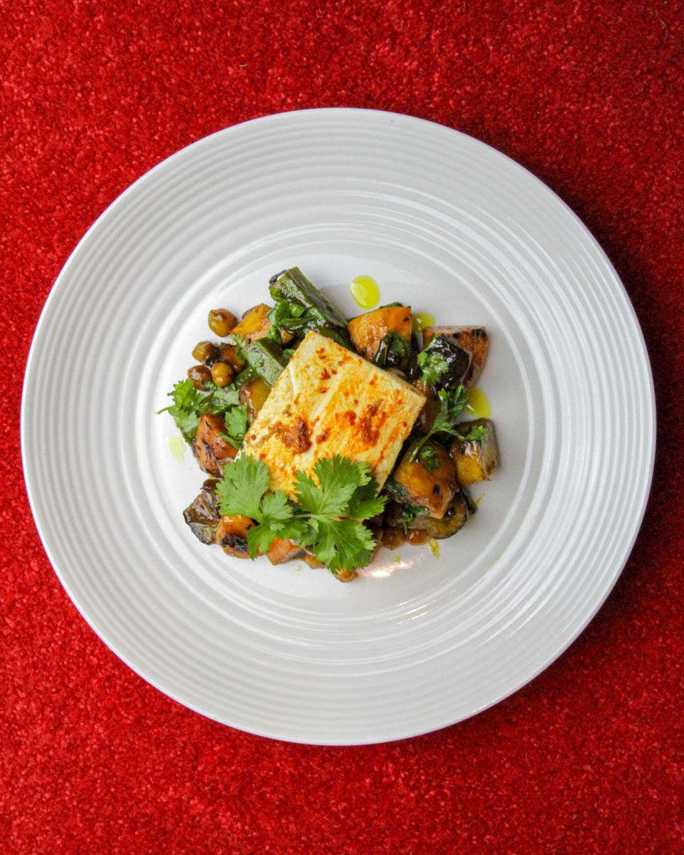 vegan Brinjal pickle vegetables and spiced tofu steak with a green garnish on a white plate against a red background