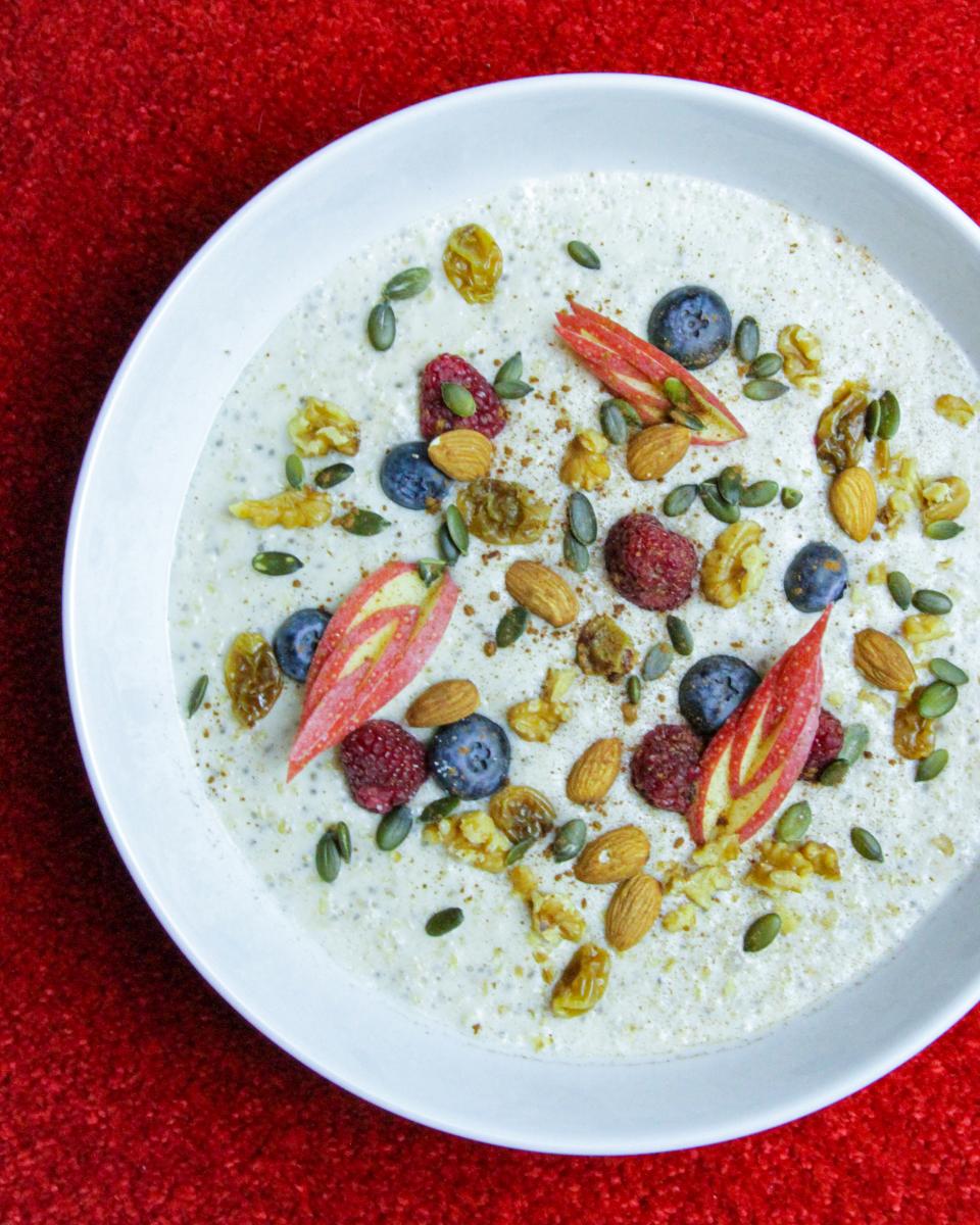 vegan breakfast porridge with nuts and fruit in a white bowl on a red background