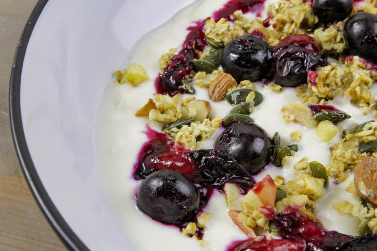 close up of vegan yoghurt and granola with cherries and seeds in a white bowl