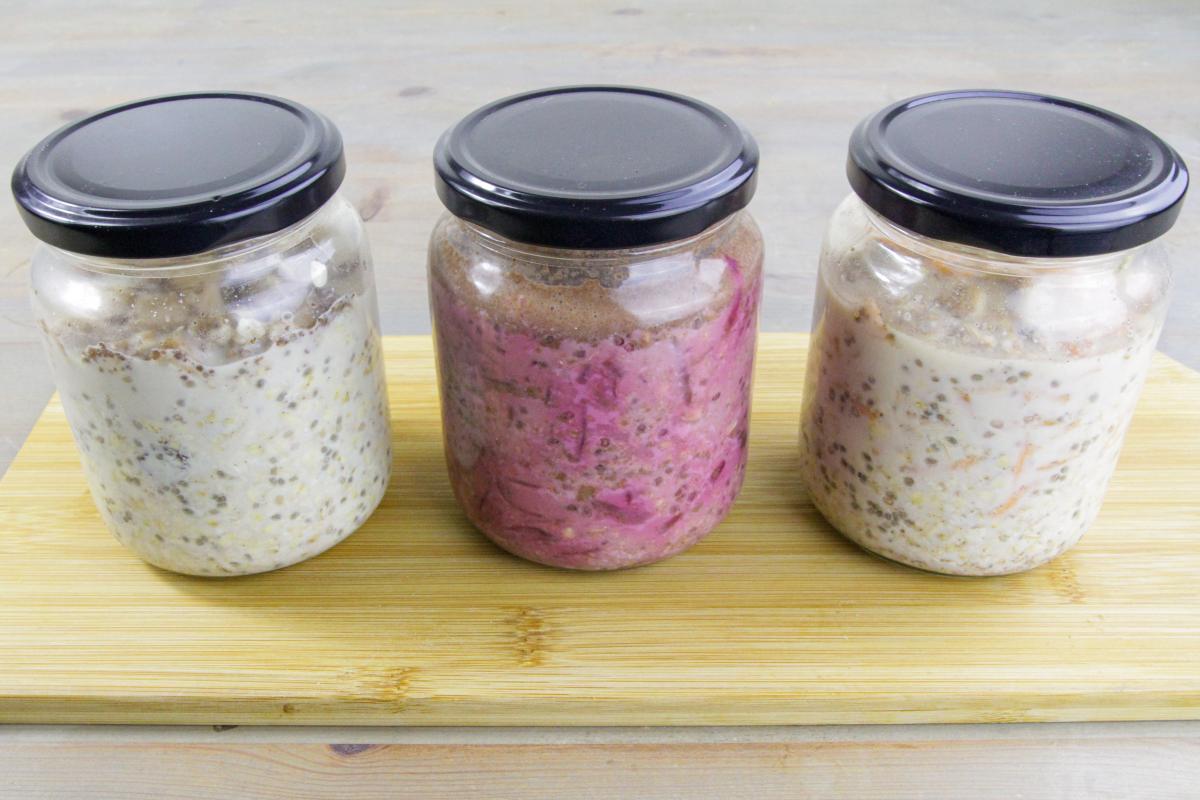 vegan overnight oats in three flavours in three different jars on a wooden board against a grey background