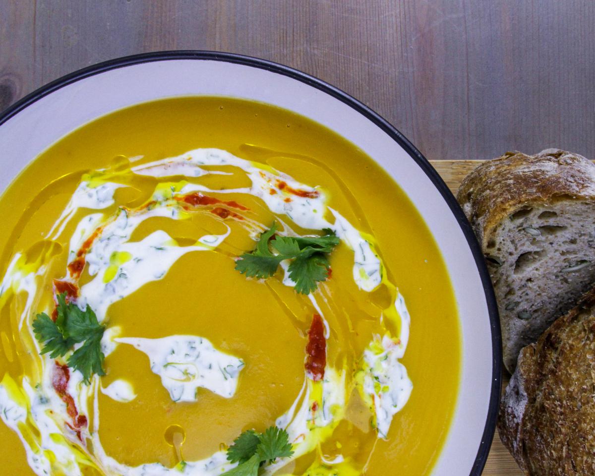 vegan sweet potato, butter bean and chilli soup in a white bowl with a blue edge with slices of thick brown bread against a grey/purple background