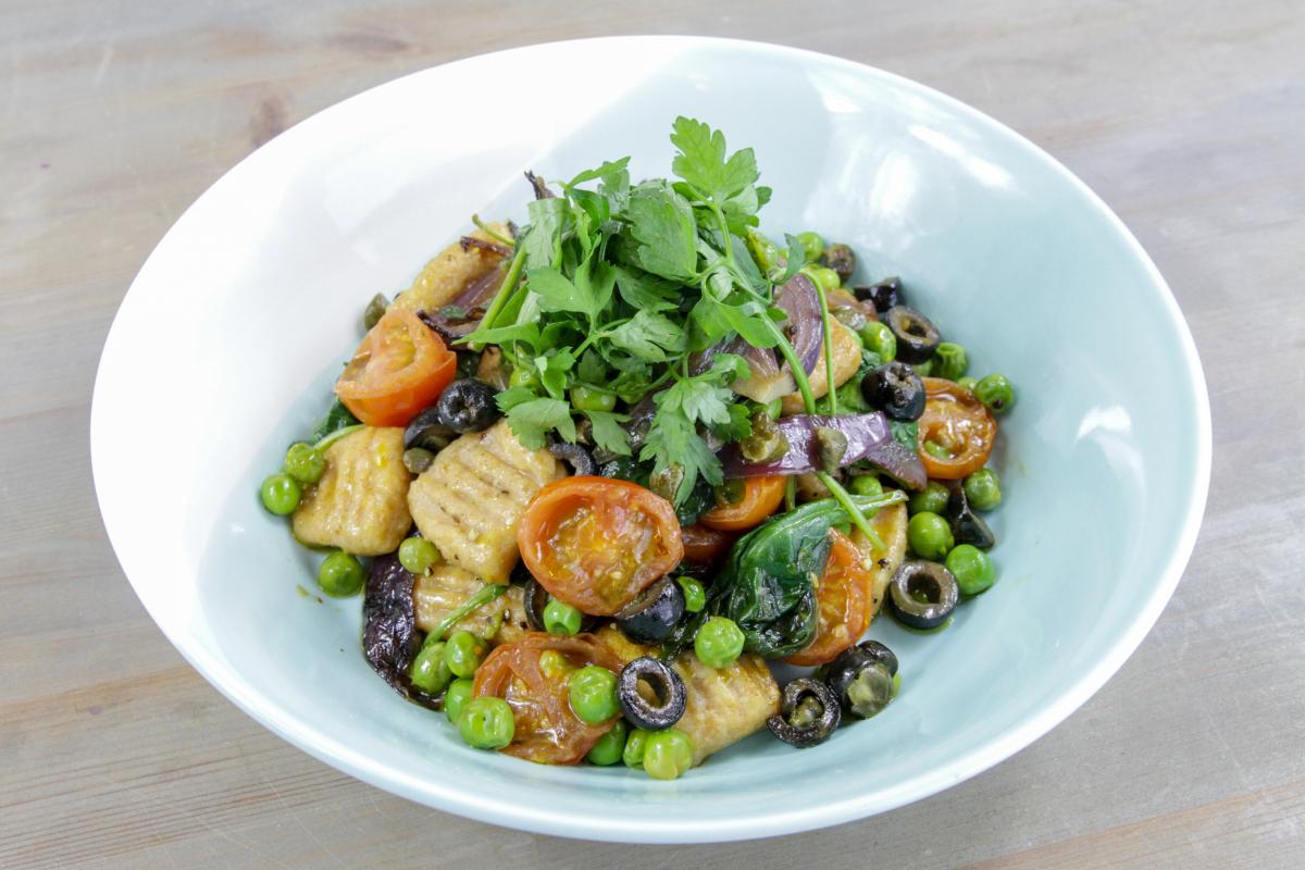 vegan sweet potato gnocchi in a white bowl with vegetables and a green garnish against a grey background