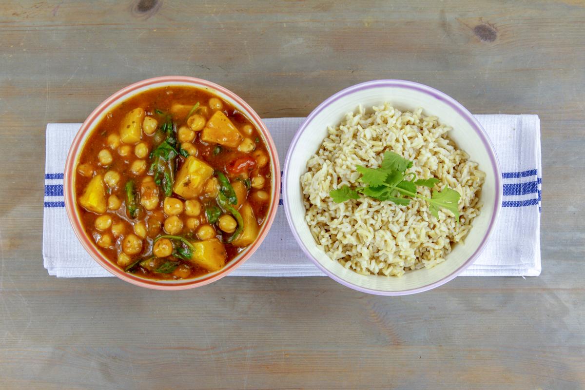 vegan pineapple chana masala in a bowl with a red edge and a bowl of rice in a bowl with a blue edge both on a kitchen cloth with blue lines on a grey surface