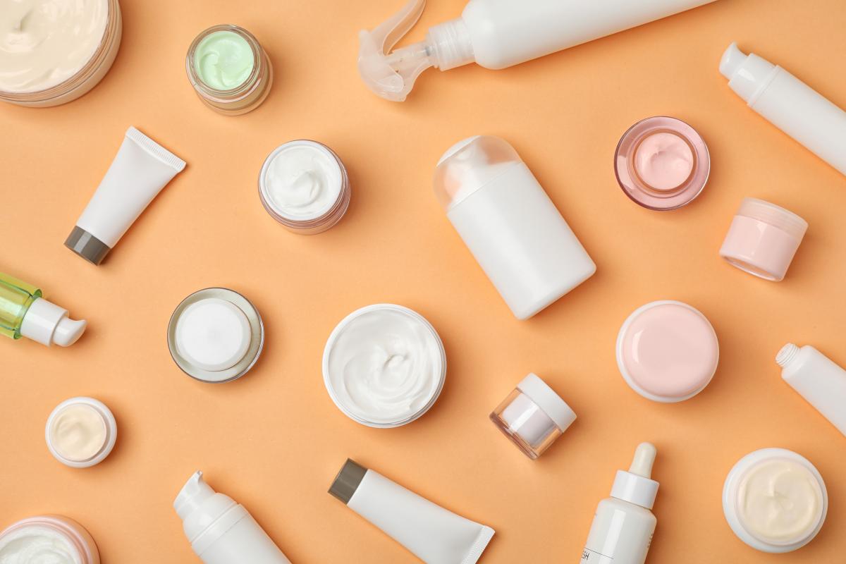 Plain cosmetics pots containing product, scattered across a peach coloured background.