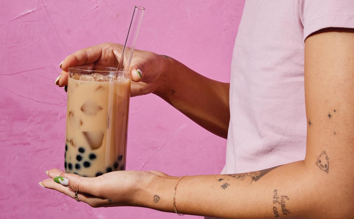 A cropped image of a person holding a glass of bubble tea against a pink background.