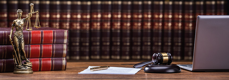 A desk with legal books, a statue of Lady Justice and a gavel.