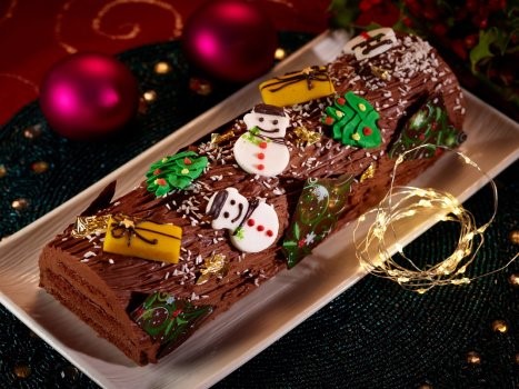 Vegan chocolate log docorated with snowmen and christmas trees served on a rectangle platter.