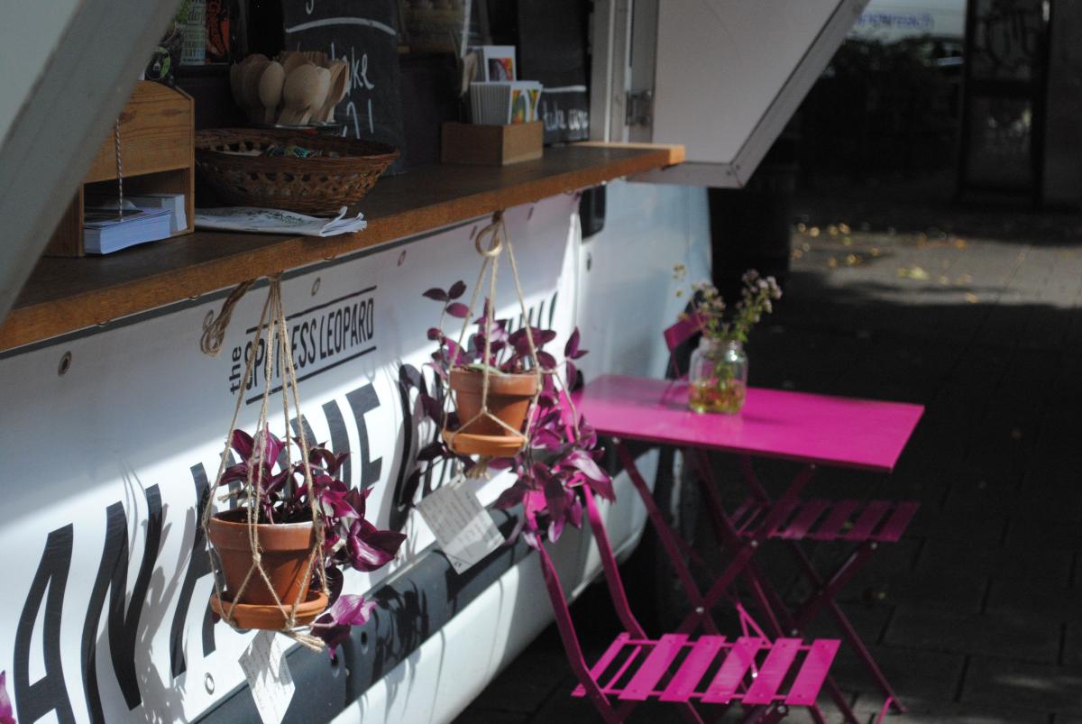 Close up of pink metal table and chairs outside of food van with hanging plant pots 