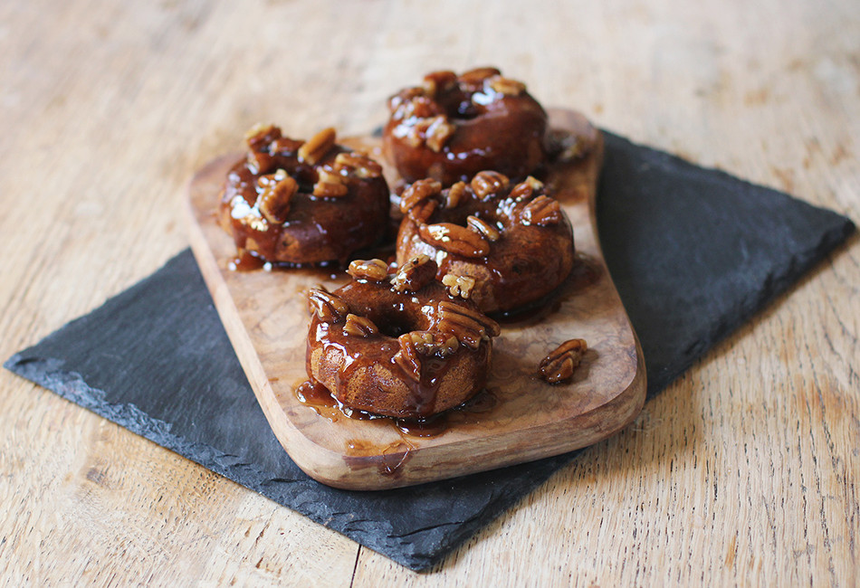 Four banana donuts topped with caramel and walnuts, served on a wooden board
