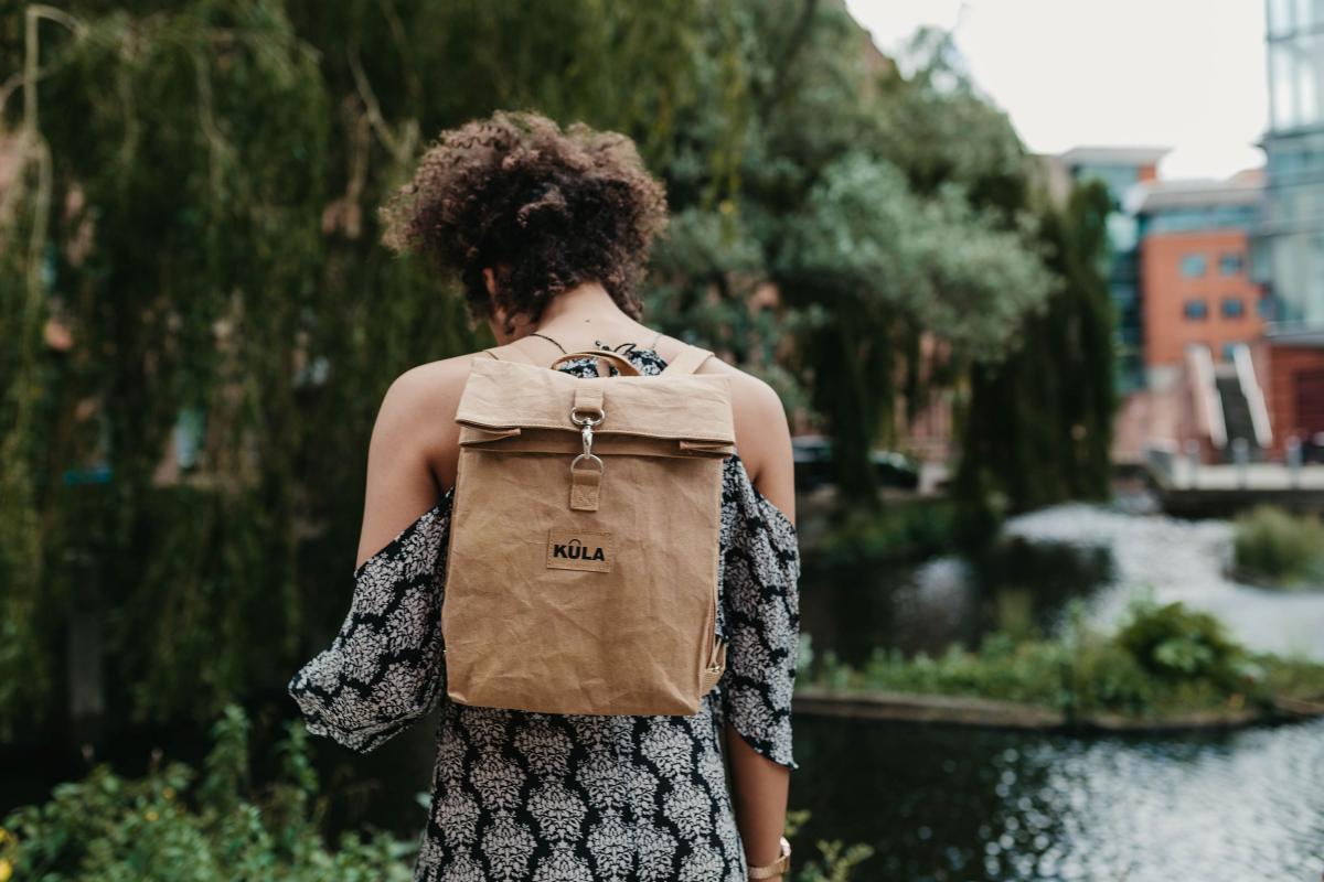 Woman stood in front of greenery with lake in front of her with backpack on