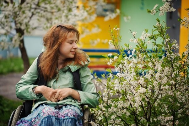 A young woman in a wheelchair smiling at some flowers in the street