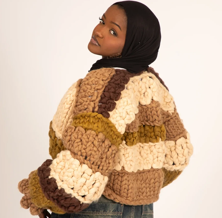 A photograph of a woman looking back at the camera, wearing a Shone knitwear top