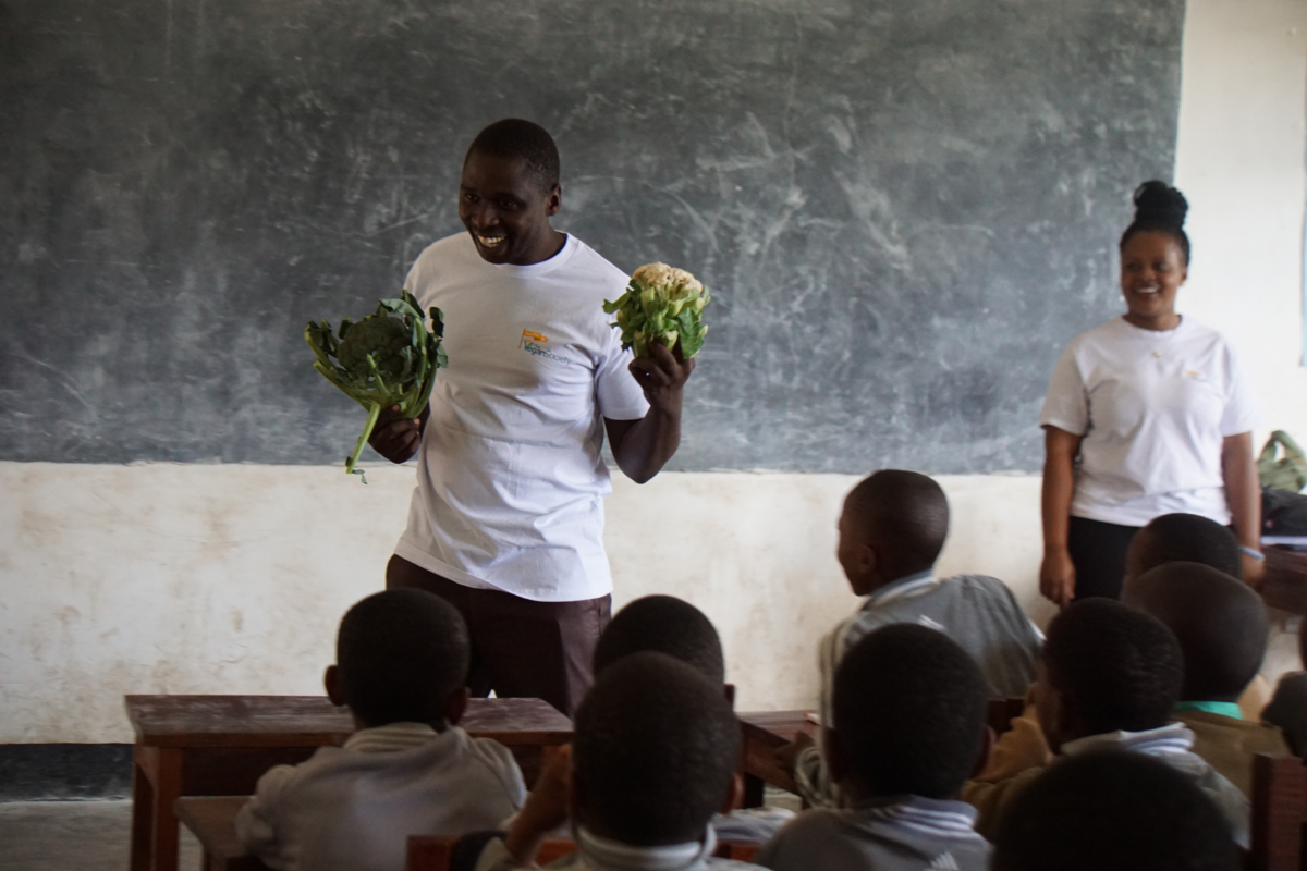 image of teacher in Tanzania talking to students about veganism holding vegetables