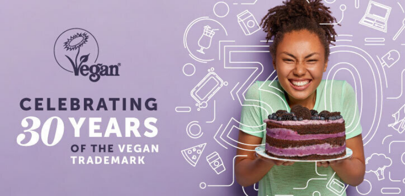 a girl holding a chocolate and berry cake against a lilac background, the number 30 over the image with text to the left reading "celebrating 30 years of the Vegan Trademark"