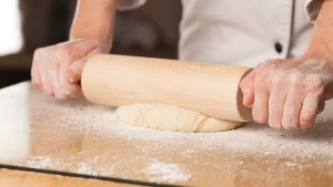 Person rolling vegan pastry with rolling pin on a surface covered in flour