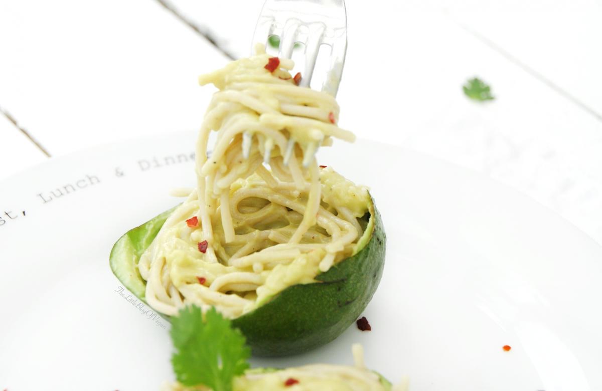 Half an avocado on a plate filled with creamy spaghetti, partly raised and twisted around a fork.  