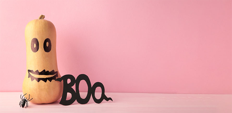 A butternut squash with a spooky halloween face drawn on, with a small plastic spider next to it and the word "Boo" cut out in black paper text. 