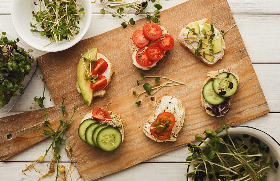 A wooden board with slices of bread with avocado, tomato and herbs on.